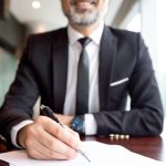 Close-up of businessman doing paperwork. Boss signing agreement or examining document at table. He writing in paper. Report concept